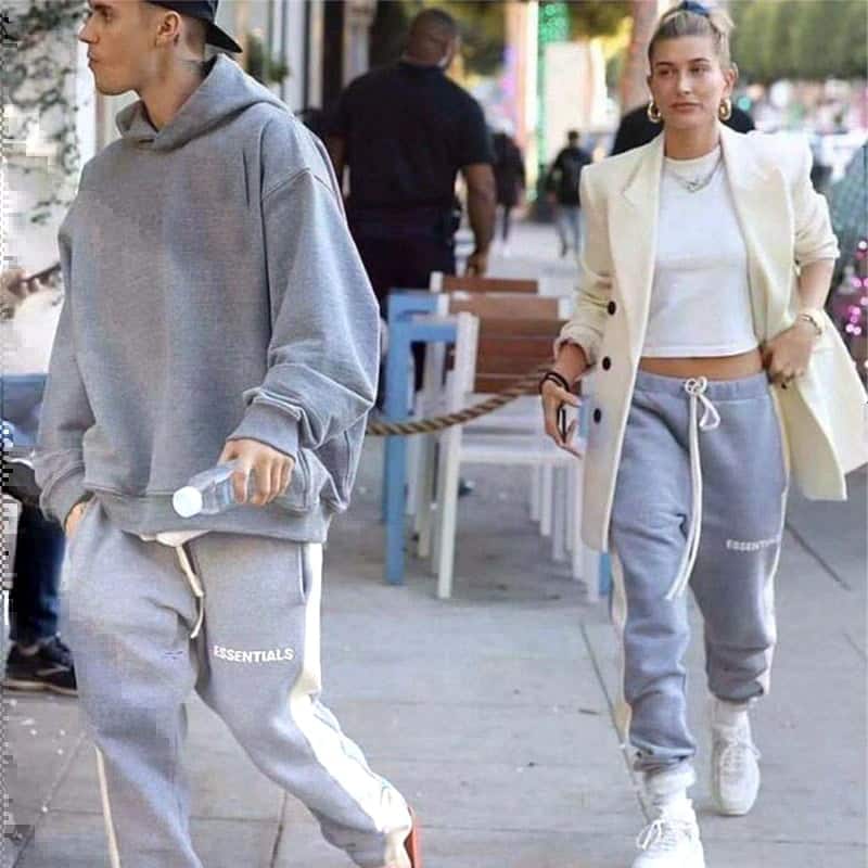 Comfy Fear of God Essentials tracksuits worn by a young man and woman in casual streetwear style.